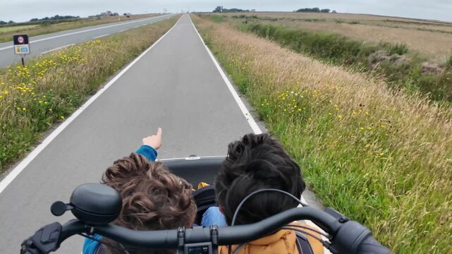 Point of view shot showing two young children sitting in the front of a cargo bike, enjoying a family outing on a dedicated cycle path through the beautiful countryside