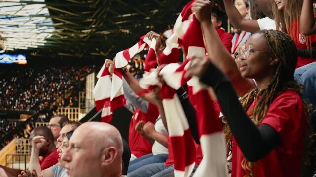 Passionate football supporters cheering loudly in the fan section, raising scarves and singing for team support with fan scarves.