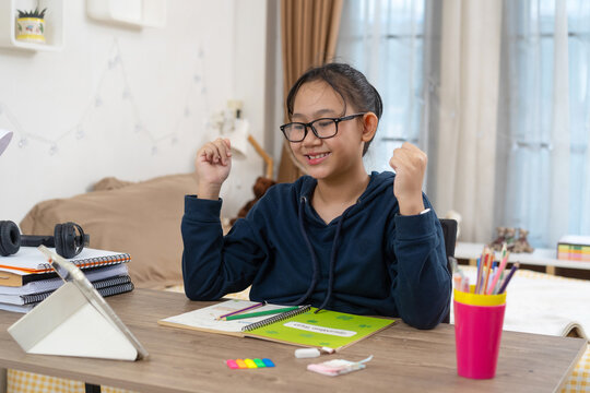 Excited youg girl Celebrating Success During Online Learning attending an online lesson on a tablet at home