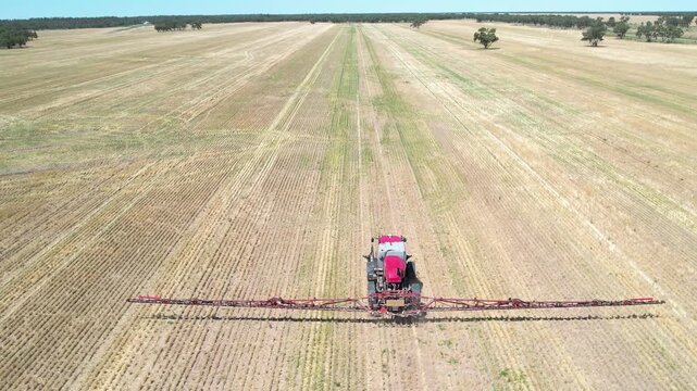 Drone following directly behind tractor sprayer centered in frame moving across symmetrical crop rows creating strong visual alignment and precision farming pattern in large dry agricultural field und