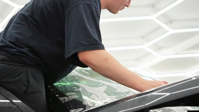 Car wrapping. Windshield protection. A man in the process of tinting the windshield. The concept of love for cars and protection. The process of installing the athermal on the windshield of a car.