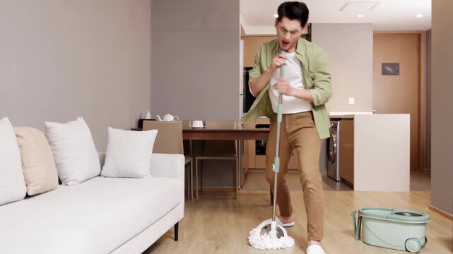 Joyful young man guy washing floor using mop dancing and singing having fun while cleaning apartment, household and housekeeping in positive mood, domestic work, householding, male cleans house