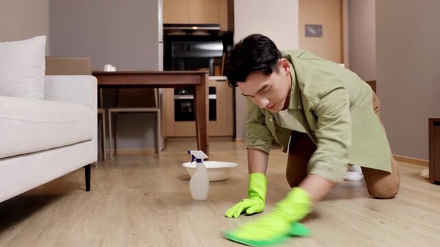 Concentrated young man doing household chores washing floor using spray detergent supplies cleaning, wrings rag, uses it to clean floor in bright modern room, demonstrating housekeeping task daily