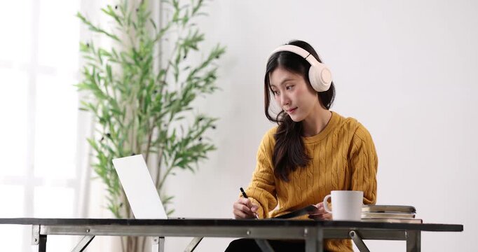 Young asian woman wearing headphones and studying online, learning new skills from home, focusing on virtual education with a laptop, happy to be collaborating remotely