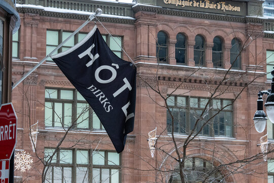 MONTREAL, CANADA, 24 December 2025 : Winter street scene, hotel flag, historic building, snowy day, urban architecture, birch trees, streetlight, stop sign