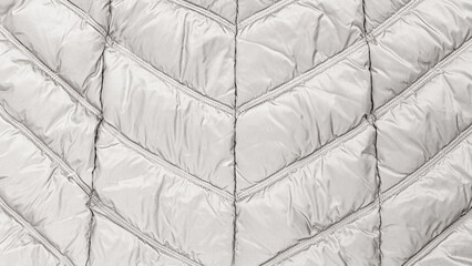 Close-up view of a light gray puffer jacket with quilted pattern and sleek design in a soft fabric setting © Fleuronica