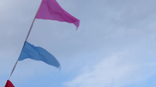 Colorful festival bunting flags waving rapidly in a strong wind against an overcast cloudy sky background