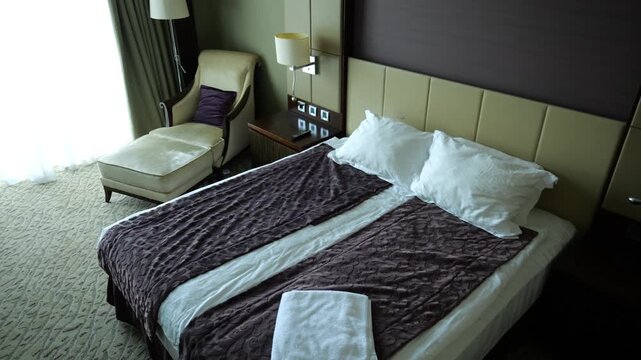 View of modern hotel room interior with neatly arranged bed, soft day lighting and comfortable furniture. Cozy accommodation space designed for relaxation, travel and hospitality service