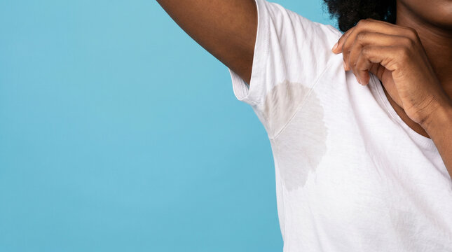 Close up of a Black woman showing a large sweat stain under her armpit on a white t-shirt. Hyperhidrosis, body odor, and deodorant failure concept. Copyspace