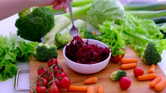 Grated beetroot in white plate with fresh vegetables and female hand holding fork