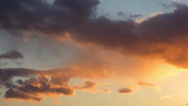 Cloudy evening sky. Dramatic skyscape at sunset with dark purple and gray clouds above vibrant gold yellow and orange hues, indicating a low sun partially obscured by clouds. Golden hour. 4k footage.
