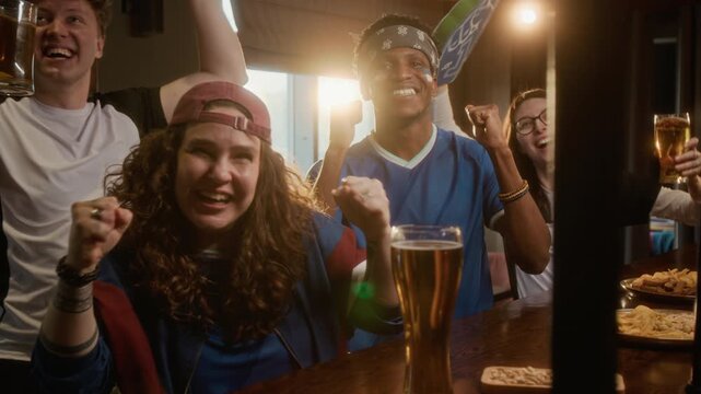 Handheld POV shot of excited young multiethnic sports fans in team jersey sitting at bar counter raising arms and expressing joy together, celebrating sports win after watching game