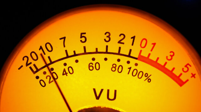 Close up of vintage analog VU meter dial with warm orange glowing light for audio level measurement in recording studio