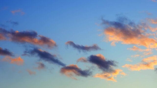 Cloudy evening sky. Dramatic skyscape at sunset with dark purple and gray clouds above vibrant gold yellow and orange hues, indicating a low sun partially obscured by clouds. Golden hour. 4k footage.