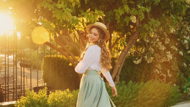 Cheerful happy joyful young woman red long loose hair fly wind throws. cute Girl spinning dancing hands raised to magic sun light flare sunset. Beauty Smiling face. summer nature reen trees. boat hat 