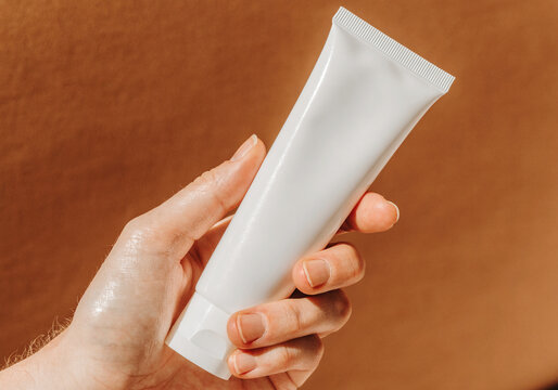 Minimalist white skincare tube mockup held in hand under warm natural light.