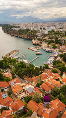 Fototapeta premium drone aerial Antalya old town Kaleici, showing the ancient Roman harbor, traditional red tiled roofs, steep cliffs and modern urban skyline, Turkey