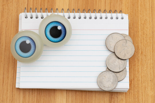 Blank spiral notebook of index cards with big blue eyes with money on wood desk