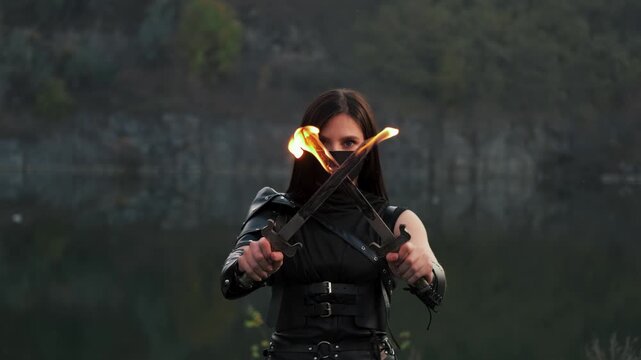Portrait fantasy woman warrior assassin holds dancing with two burning blade daggers in hands, flame fire. Dancer hiding face behind mask. Armed sexy girl. Black costume. Halloween concept 4k footage