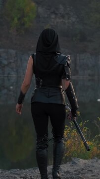 unrecognizable silhouette person fantasy woman warrior assassin holds dagger in hands walks at night nature. back Rear view armed girl. Black leather costume hood on head. Ninja soldier with sword 4k 