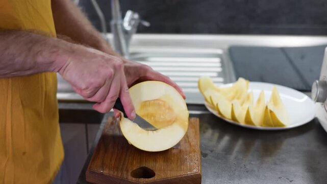 Man cutting ripe yellow melon into slices on wooden board in modern HD video kitchen Full