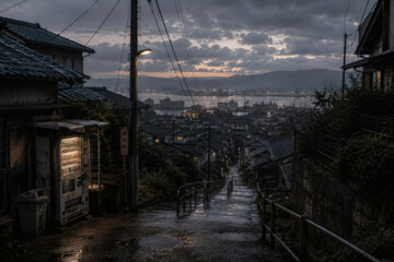 Fototapeta premium Quiet rainy hillside street overlooking a Japanese harbor town at dusk
