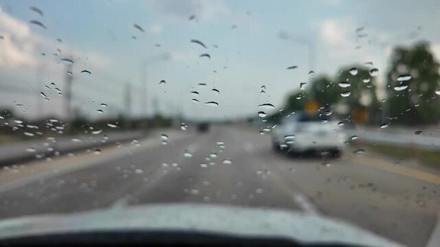 Raindrops on Windshield View: A blurred perspective from inside a car, showing raindrops clinging to the windshield, obscuring the view of a wet road and passing vehicles.