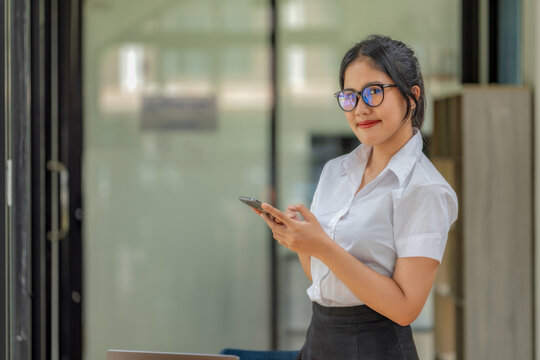 Happy young Asian woman with glasses smiling while texting on smartphone.