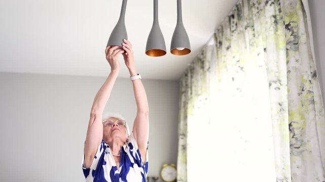 Senior woman installing light bulb into hanging lamp
