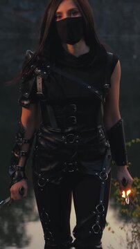  fantasy woman warrior assassin holds burning fire dagger in hands walks at night nature. Gothic sexy armed girl. Black leather costume mask hides face. Ninja sword knife. 4k footage. river rocks