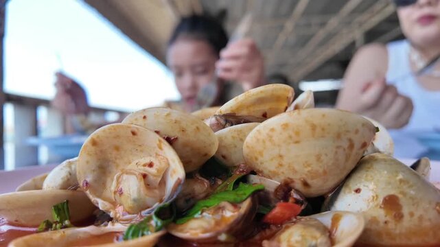 Gourmet Clam Dish: A close-up shot showcases a steaming platter of savory clams in a rich, aromatic sauce, served at an outdoor dining establishment.