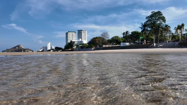 Coastal Cityscape: A serene beach meets a bustling cityscape under a clear blue sky, with calm waters reflecting the modern architecture and lush greenery.