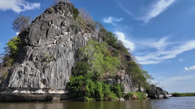 Majestic Limestone Cliff Overlooking Water: A striking limestone cliff face, sculpted by nature, rises dramatically from the calm waters of a bay. Lush green vegetation clings to its rocky surface.