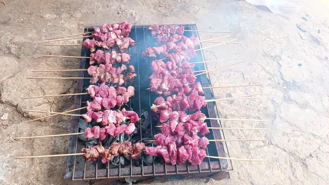 Cooking traditional Indonesian meat satay over burning charcoal grill.