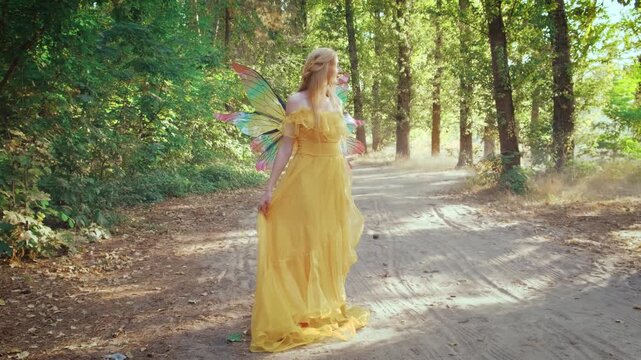 Silhouette happy fantasy woman forest fairy back rear view. Girl elf princess enjoying walking on dirt road forest path. Yellow dress costume pixie butterfly wings. Green leaves tree, summer nature.