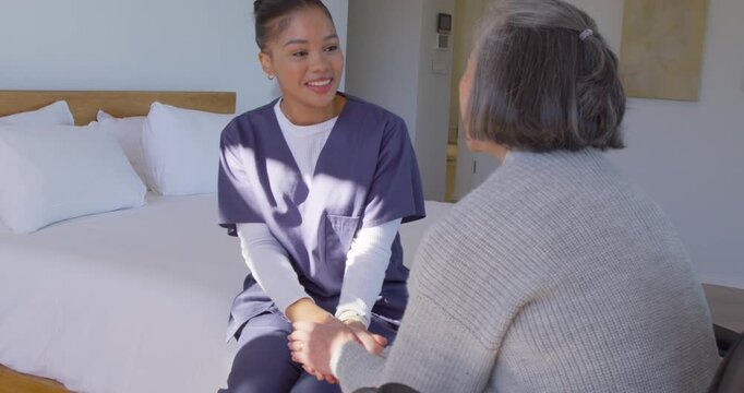 Caregiver in navy scrubs initiating hand-holding with senior client, conversing on bed to comfort