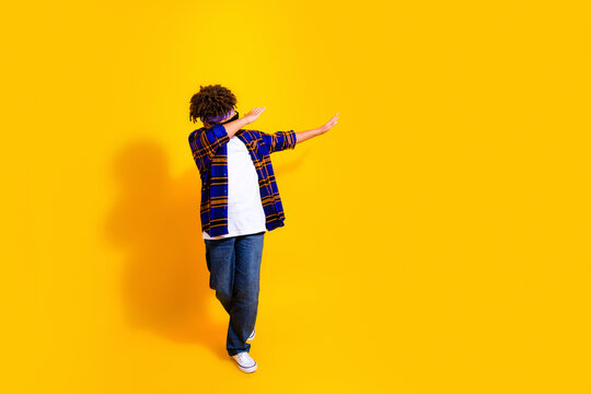Teenager dabbing and dancing in casual flannel shirt and jeans against a bright yellow background