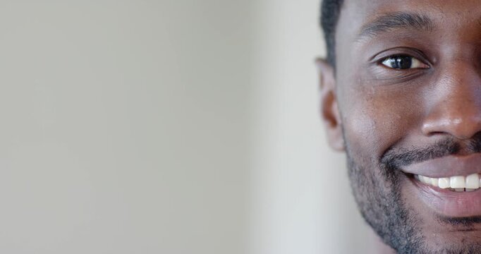 Mid adult African man holding neutral face, slowly smiling toward camera in bright room, copy space