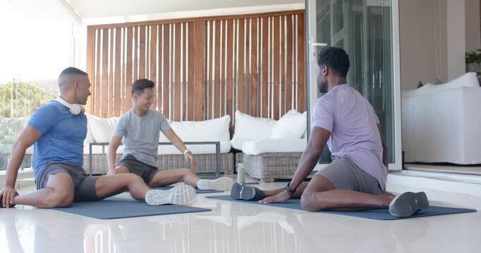 Diverse male friends warming up and stretching on tiled patio mats, reaching for feet, smiling