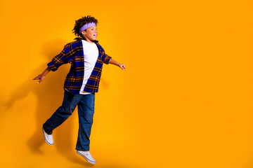 Obraz premium Happy boy jumping in casual clothes against a vibrant orange background, midair expression of energy, freedom and playful youth fashion