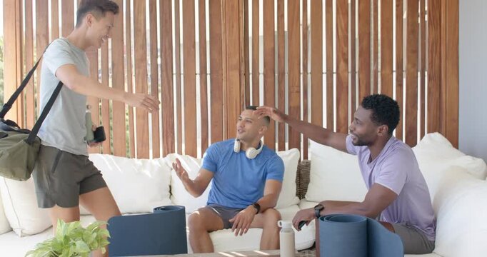 Diverse male friends greeting newcomer arriving with bag, placing water and mats on patio, prepping