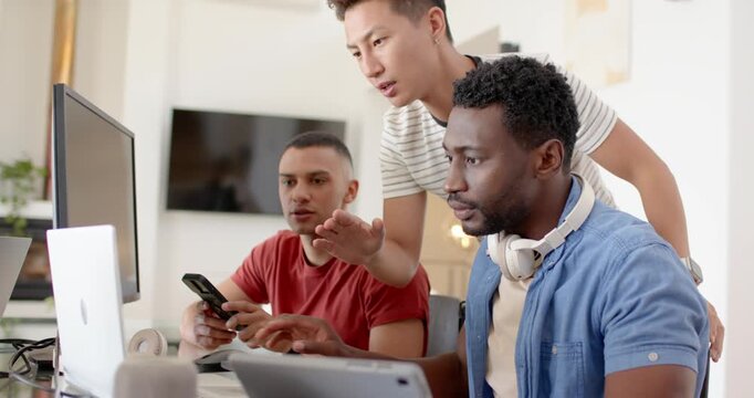 Diverse male coworkers working at desk with monitor in office, smartphone sparking debugging