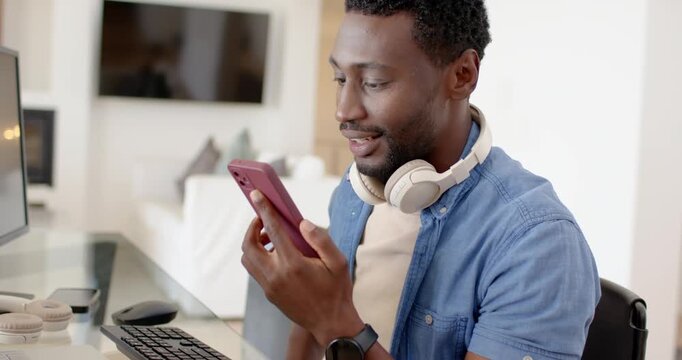 African American man reacting to audio, scrolling, speaking into pink smartphone at home office