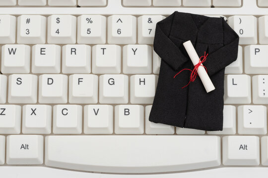 Grad gown and diploma on white computer keyboard for distance and e-learning