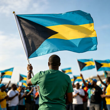 Back view of a man holding and waving the Bahamas flag high during a public holiday celebration or rally.