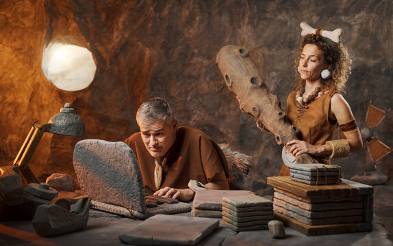 A prehistoric forewoman looms over her male employee, brandishing a large wooden club