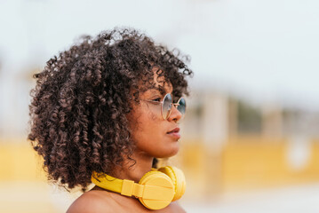 Profile portrait of young woman with curly hairstyle, sunglasses and yellow headphones outdoors © Renata Hamuda