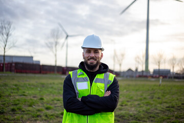 Electrical technician standing confidently at clean energy site with wind turbines, focusing on sustainable power industry © Martin