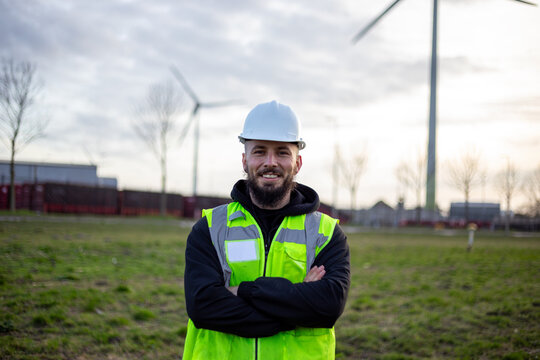 Electrical technician standing confidently at clean energy site with wind turbines, focusing on sustainable power industry