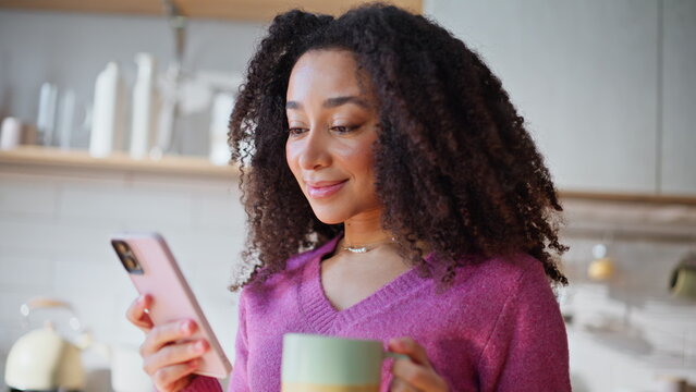 Portrait woman browsing smartphone message holding morning coffee at kitchen.